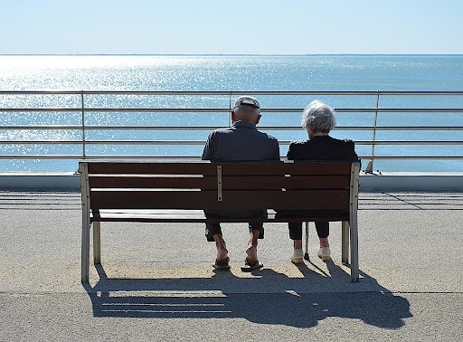 Elderly couple sitting on a bench by the ocean, symbolizing peace and security through financial planning for senior care.